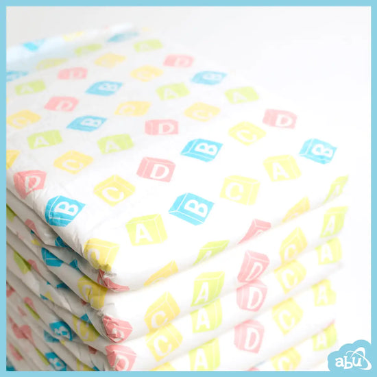 Stack of white diapers featuring colorful, alphabet-lettered building block designs in pink, blue, yellow, and green.